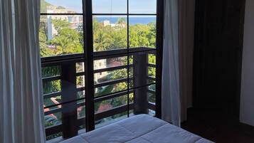 Una habitación con cama, ventanas amplias y vistas a zonas verdes y edificios.