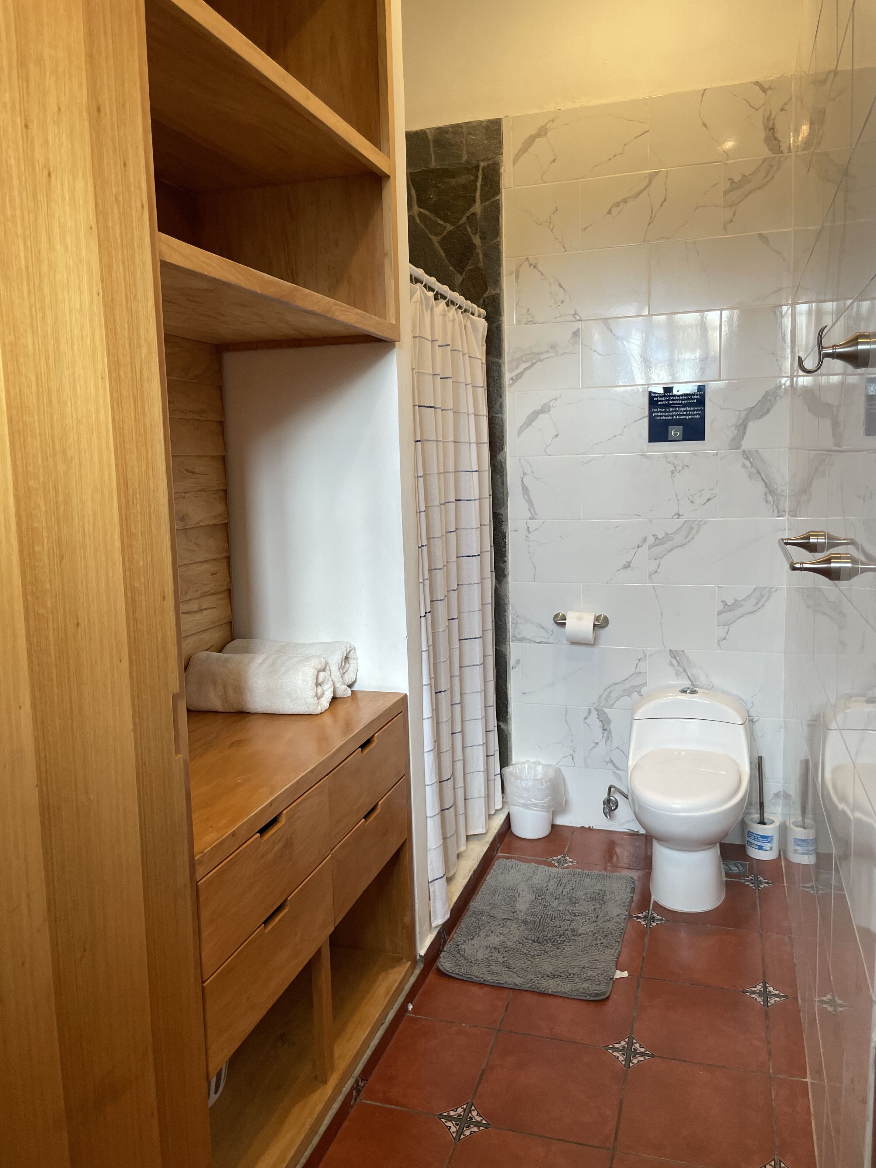A bathroom with a wooden vanity, a shower with marble tiles, and a toilet with a bidet attachment.