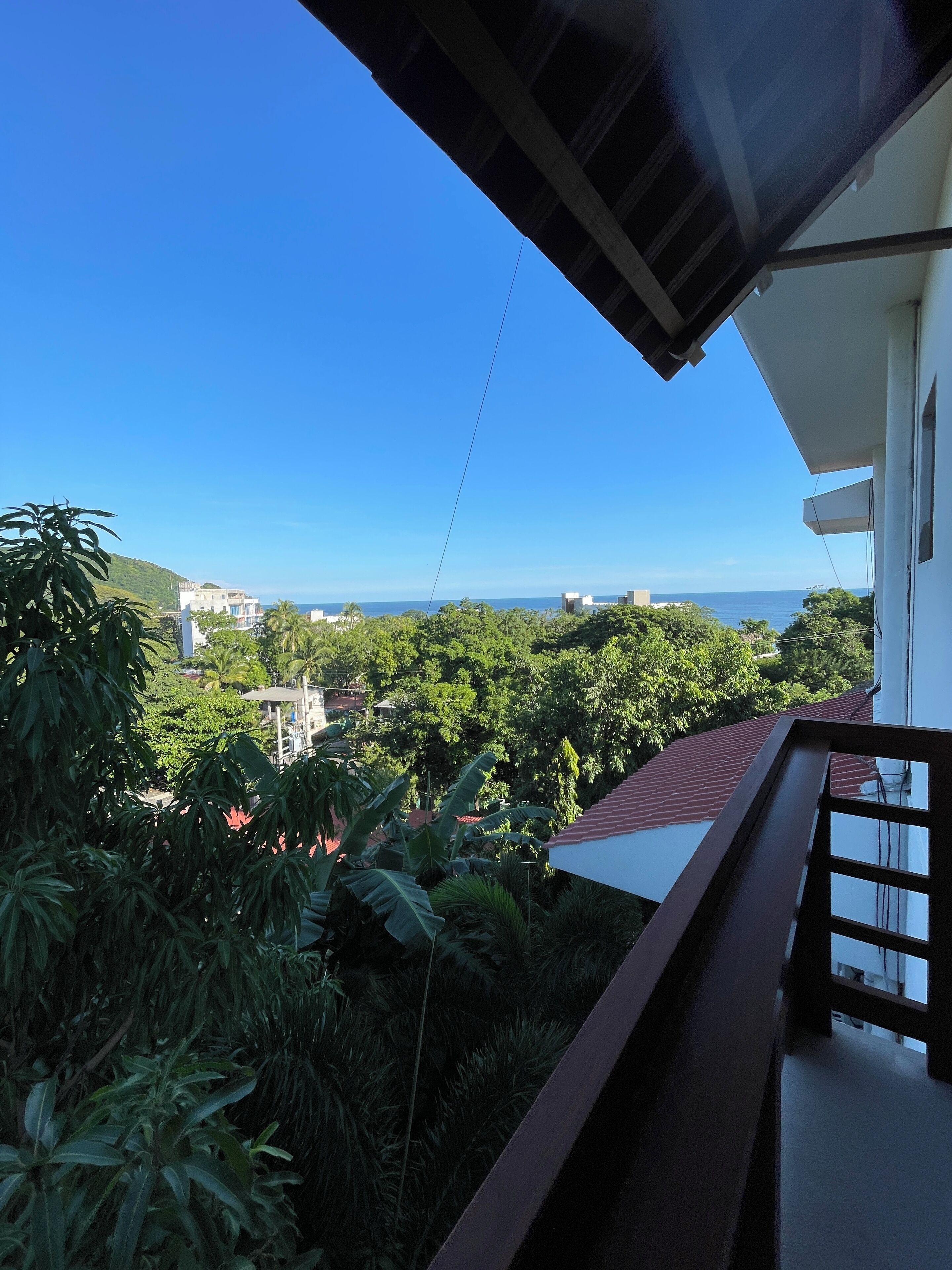 A balcony with a view of the sea and surrounding greenery.
