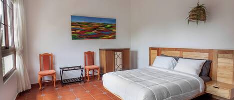 Un dormitorio con una cama, dos sillas, una mesita, un armario y un cuadro en la pared.