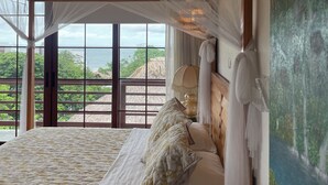 Een slaapkamer met een groot bed, een hemelbed en uitzicht op zee door grote ramen.