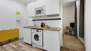 A compact kitchen with a built-in washing machine, a microwave, and a small dining area.