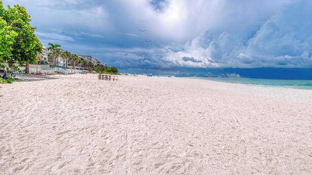 Ein weiter Sandstrand mit freiem Blick auf das Meer und einigen Gebäuden im Hintergrund.
