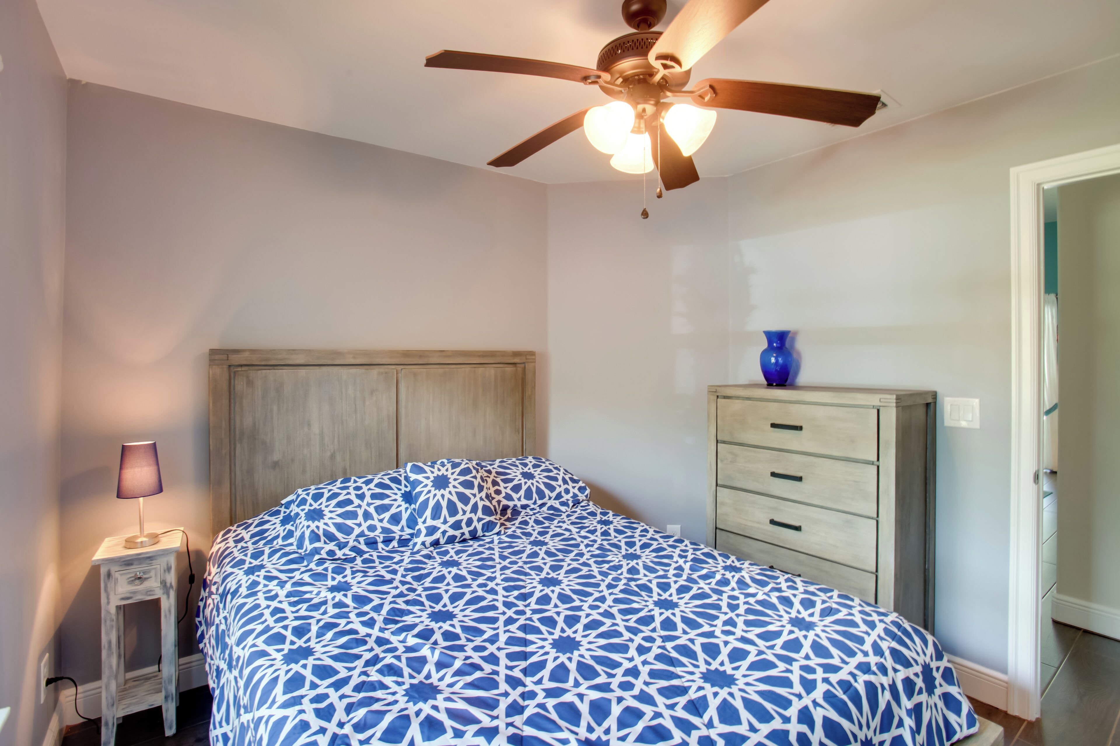 A bedroom with a bed, a nightstand, a dresser, a ceiling fan, and a door.