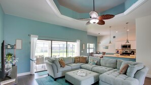 A spacious living room with a large sectional sofa, a ceiling fan, and a kitchen area in the background. - Family Retreat w/ Backyard Oasis in Cape Coral! (Cape Coral)