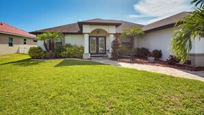A two-story house with a front porch, a well-maintained lawn, and a clear blue sky. - Family Retreat w/ Backyard Oasis in Cape Coral! (Cape Coral)