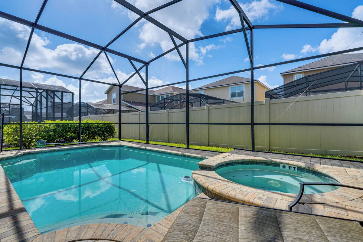 A swimming pool with a hot tub, surrounded by a metal fence and a covered patio area.
