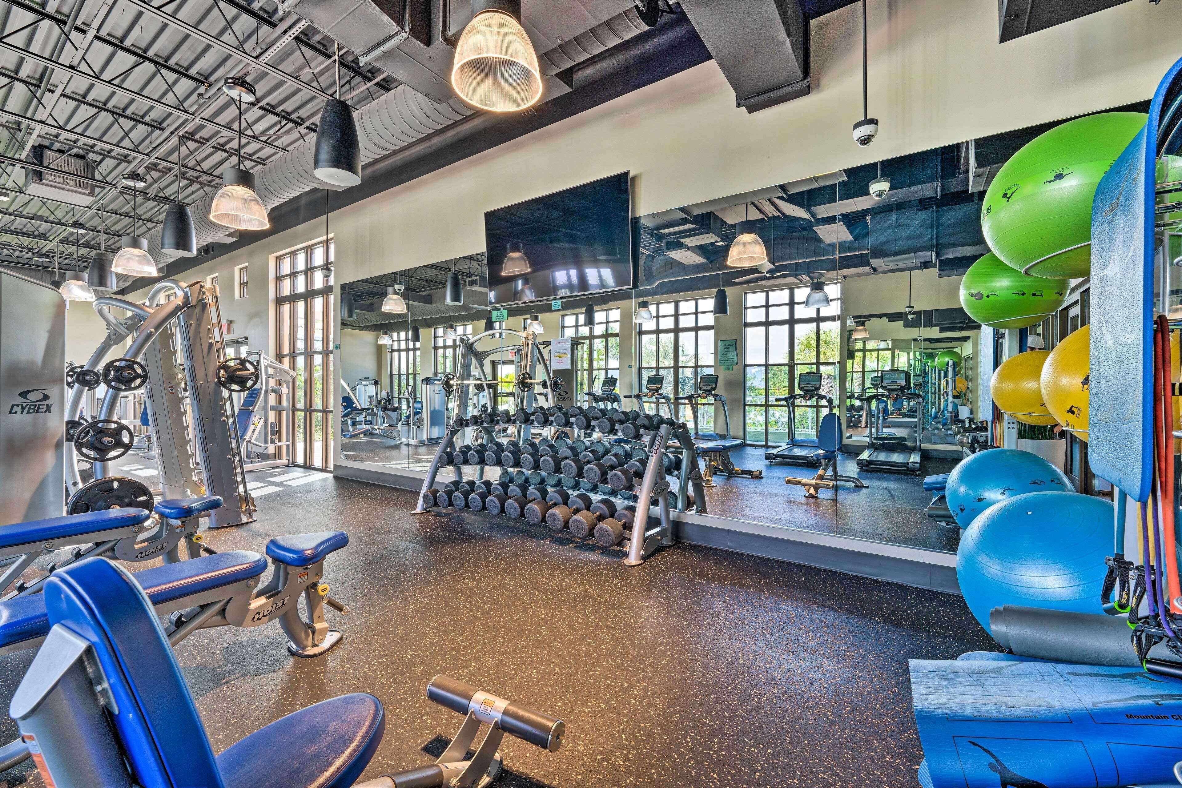Un gimnasio con equipo de ejercicio, espejos y ventanas amplias.