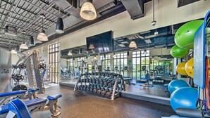 Une salle de sport équipée de matériel d’exercice, de miroirs et de grandes fenêtres.