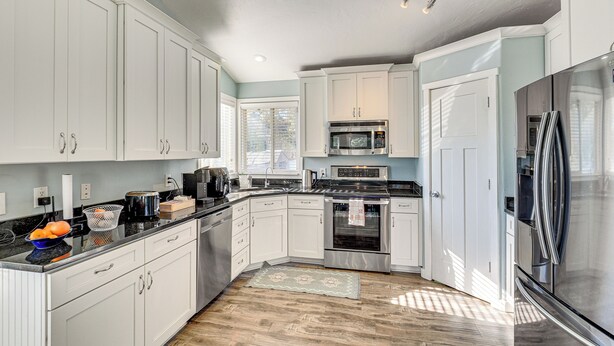 A modern kitchen with white cabinets, stainless steel appliances, and a wooden floor. - Family Home w/ Fenced Yard Between Provo & Slc! (Herriman)