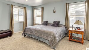 A bedroom with a bed, a nightstand, a lamp, and a window with curtains. - Family Home w/ Fenced Yard Between Provo & Slc! (Herriman)