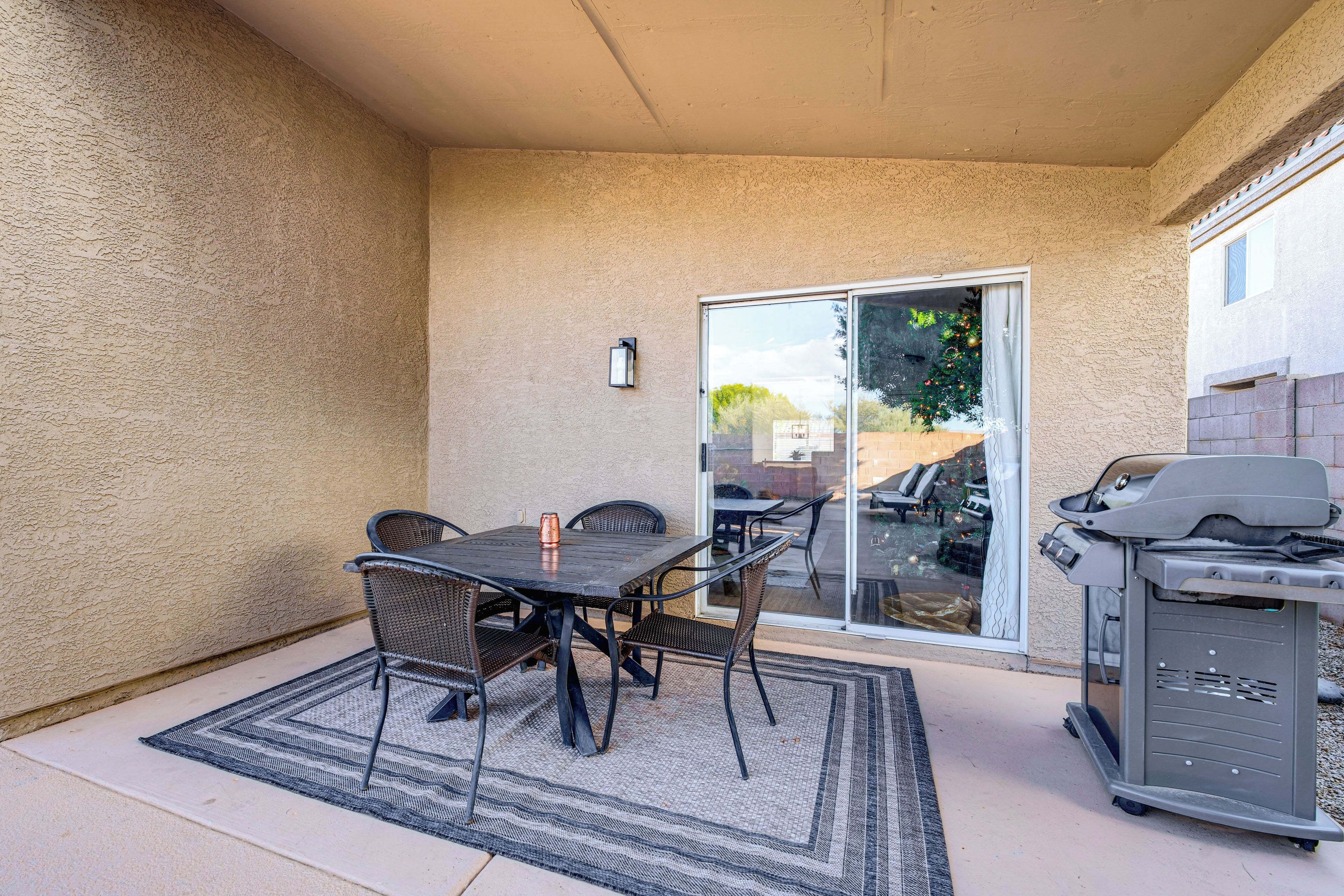 A patio with a table and chairs, a grill, and a sliding glass door leading to a backyard.