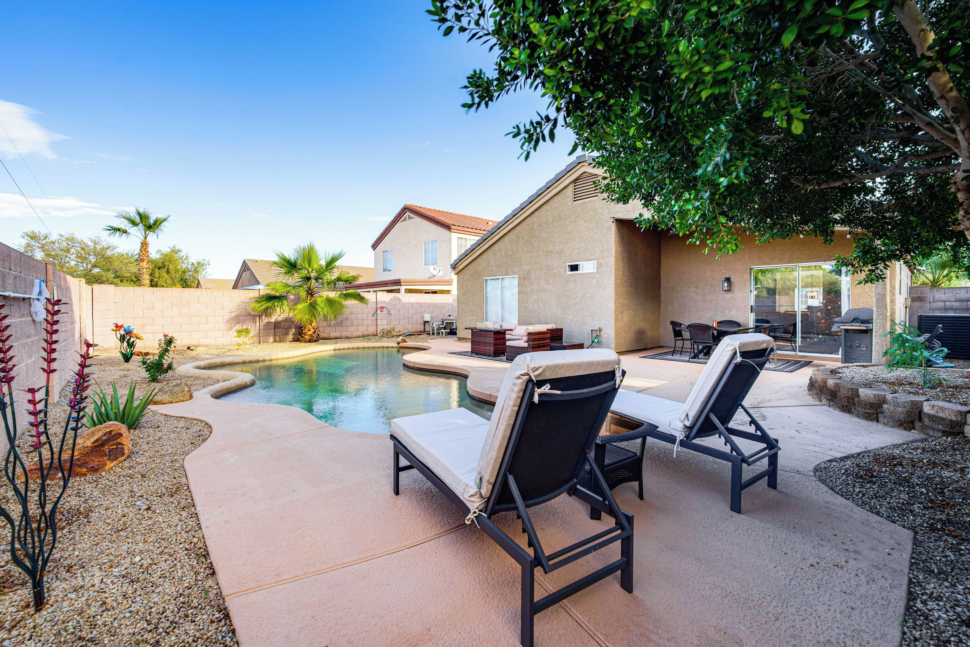 A backyard with a swimming pool, lounge chairs, and a patio area.