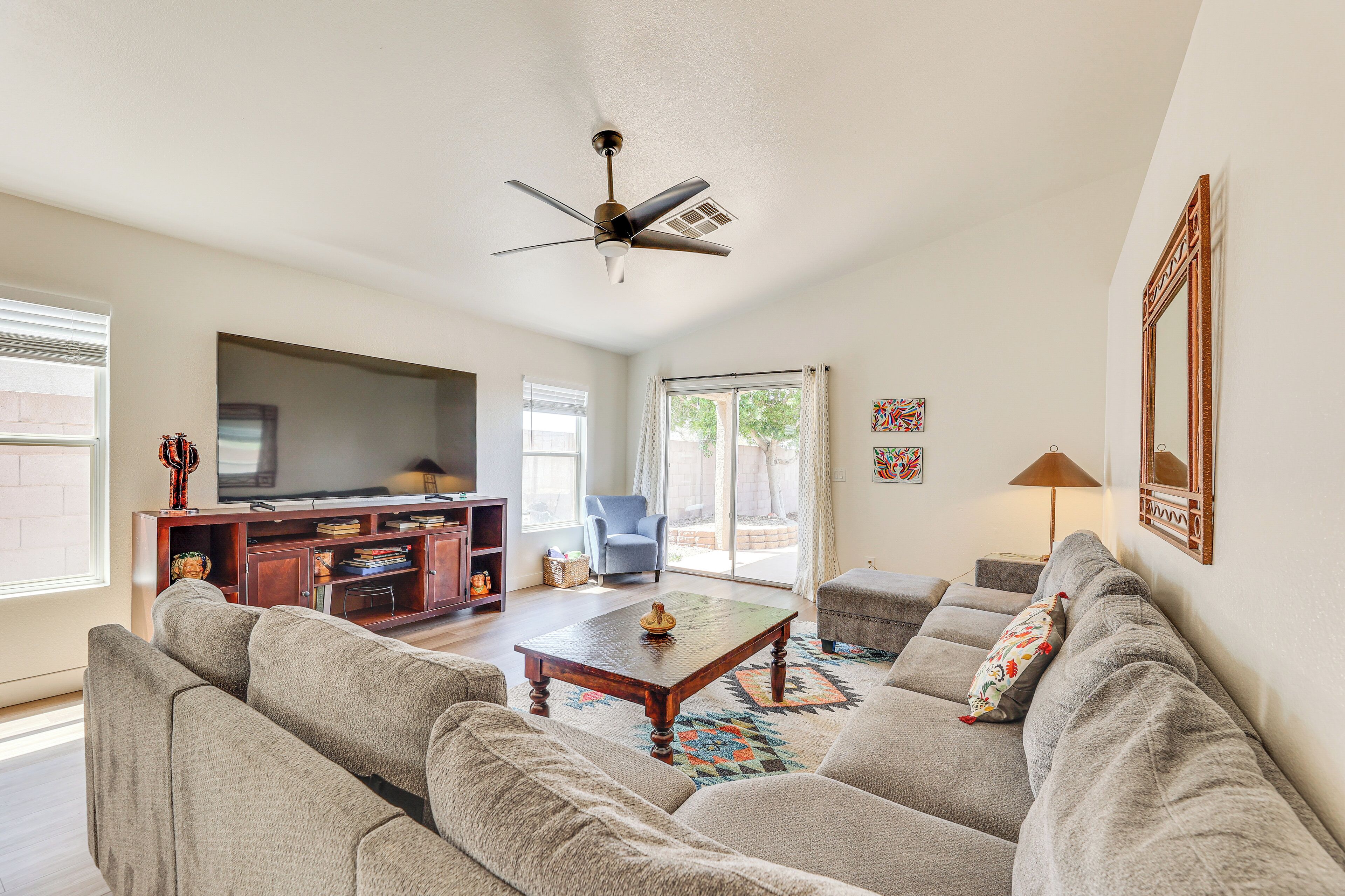 A spacious living room with a large sofa, a coffee table, and a ceiling fan. There is a television on a stand and a window with curtains.