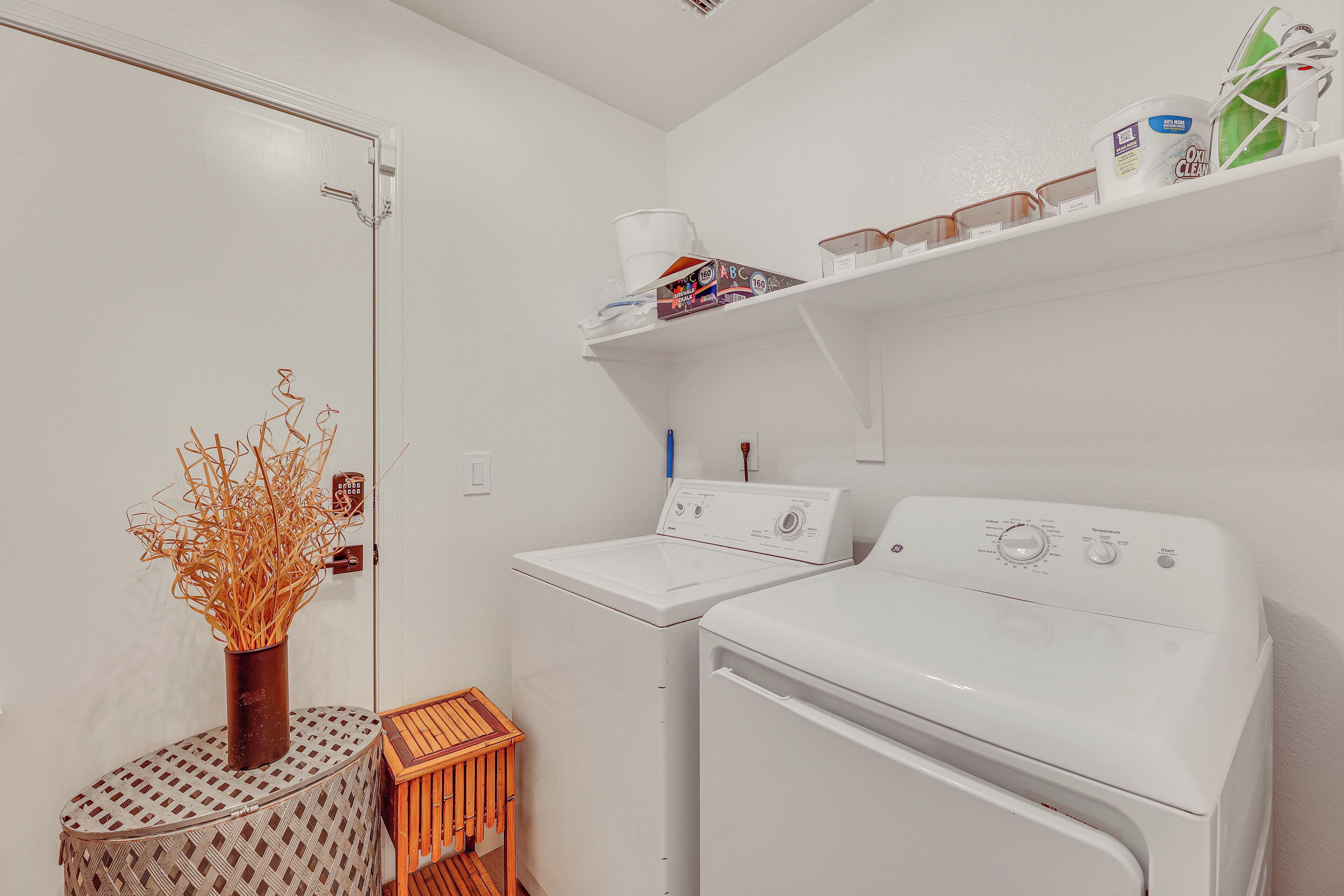 A laundry area with two white washing machines, a drying rack, a small wooden stool, and a shelf with cleaning supplies.