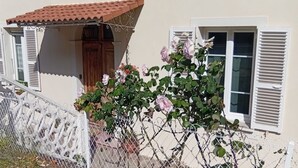 Una casa con fachada blanca, tejado de tejas rojas y una valla blanca con un portón decorativo.