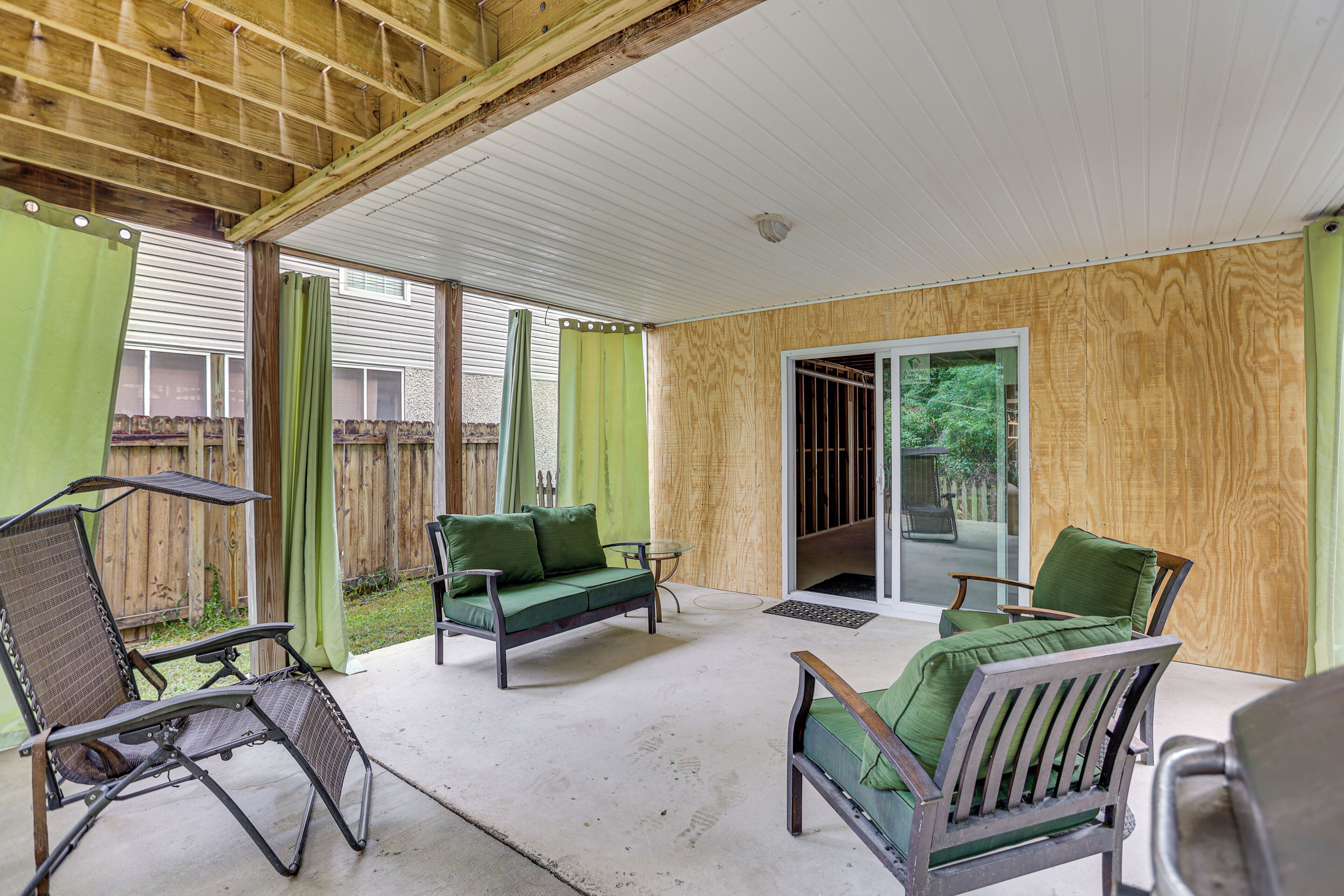 A covered patio area with a wooden ceiling, green curtains, and a sliding glass door leading to a backyard.