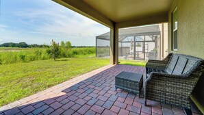 A covered patio with wicker furniture, a glass door leading to a garden, and a view of a green landscape. - Pool Access: Family Gem w/ Views in St Cloud! (St. Cloud)