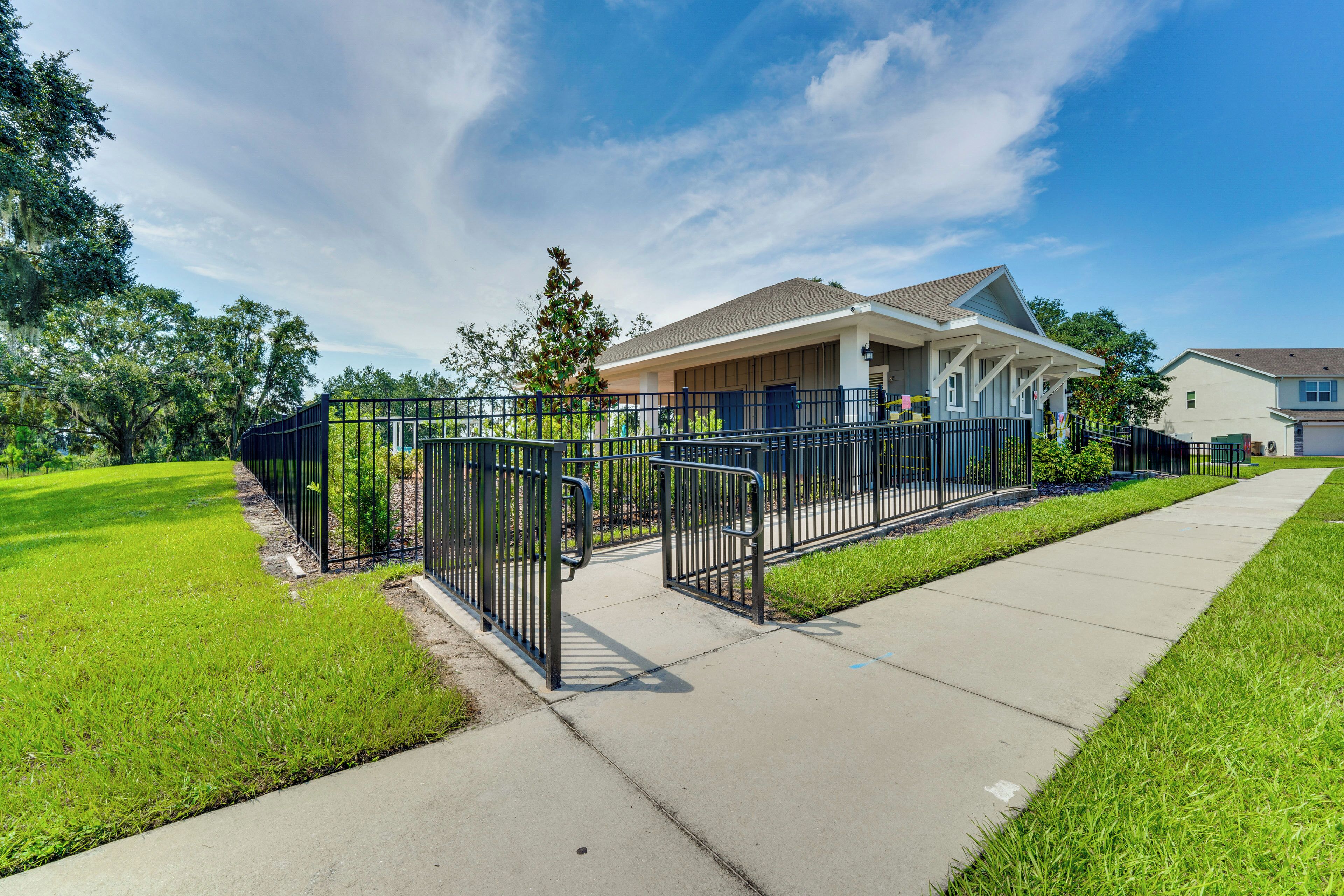 A residential house with a front yard, a sidewalk, and a metal fence.