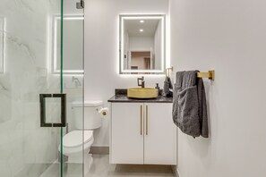 A modern bathroom with a glass shower enclosure, a white toilet, a vanity with a mirror, and a towel rack.