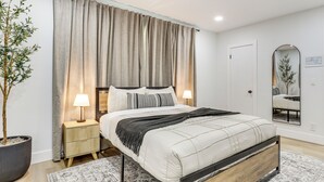 A neatly arranged bedroom with a bed, bedside lamps, a mirror, and a potted plant. - Walk to City Center: Modern Coral Springs Getaway (Coral Springs)