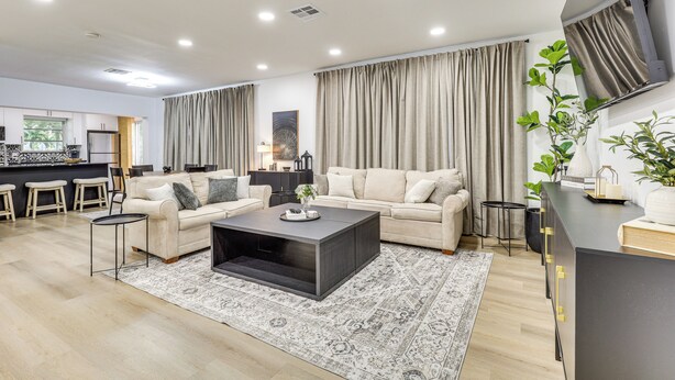 A modern living room with a sofa, coffee table, and a kitchen area in the background. - Walk to City Center: Modern Coral Springs Getaway (Coral Springs)