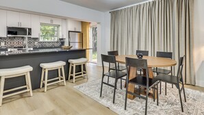 A modern kitchen with a built-in microwave, a large window, and a dining area with a round table and chairs. - Walk to City Center: Modern Coral Springs Getaway (Coral Springs)