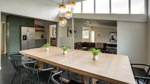 Una cocina amplia con una larga mesa de madera, electrodomésticos modernos y vista al área de estar.