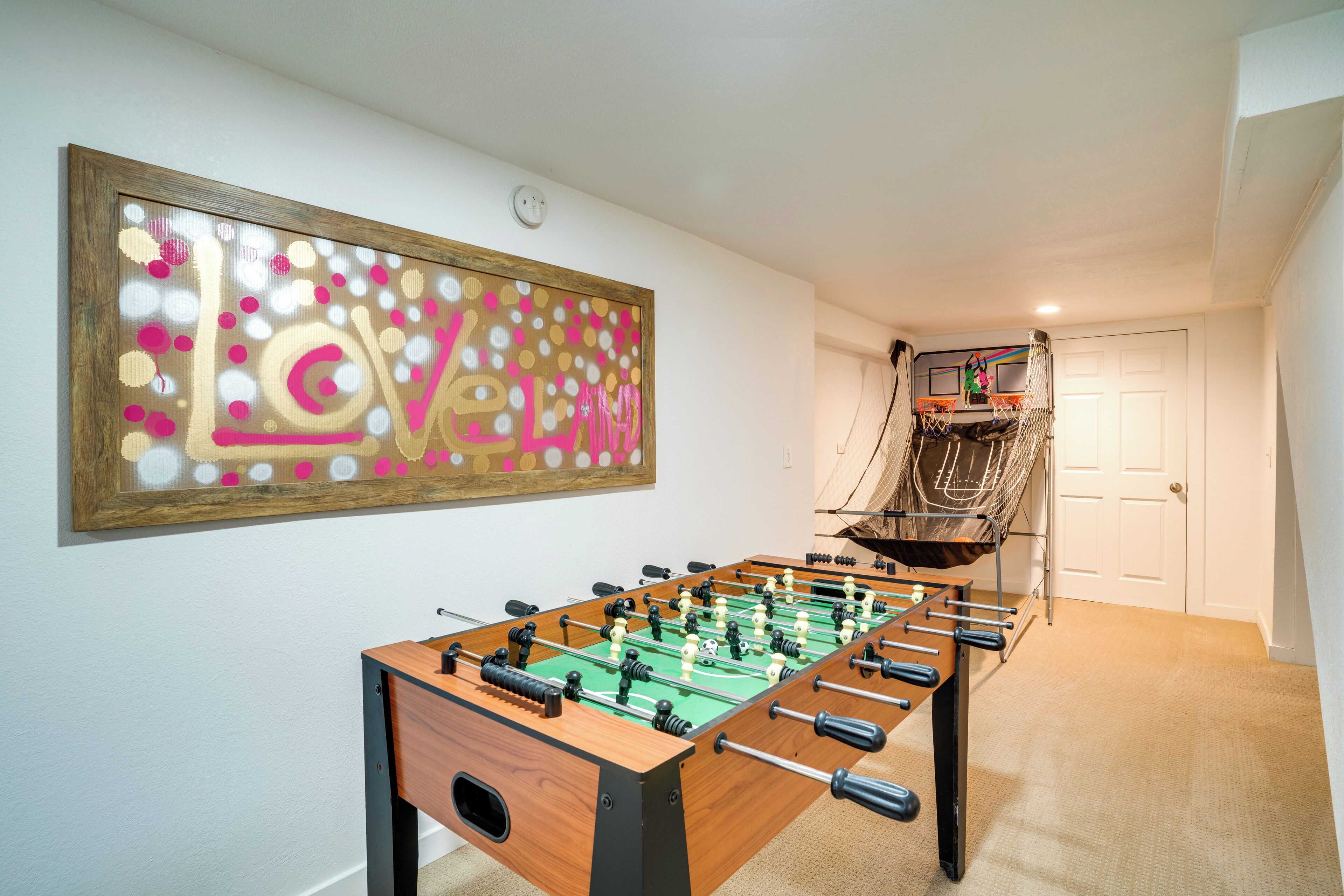 A foosball table in a room with a large abstract painting on the wall and a door in the background.