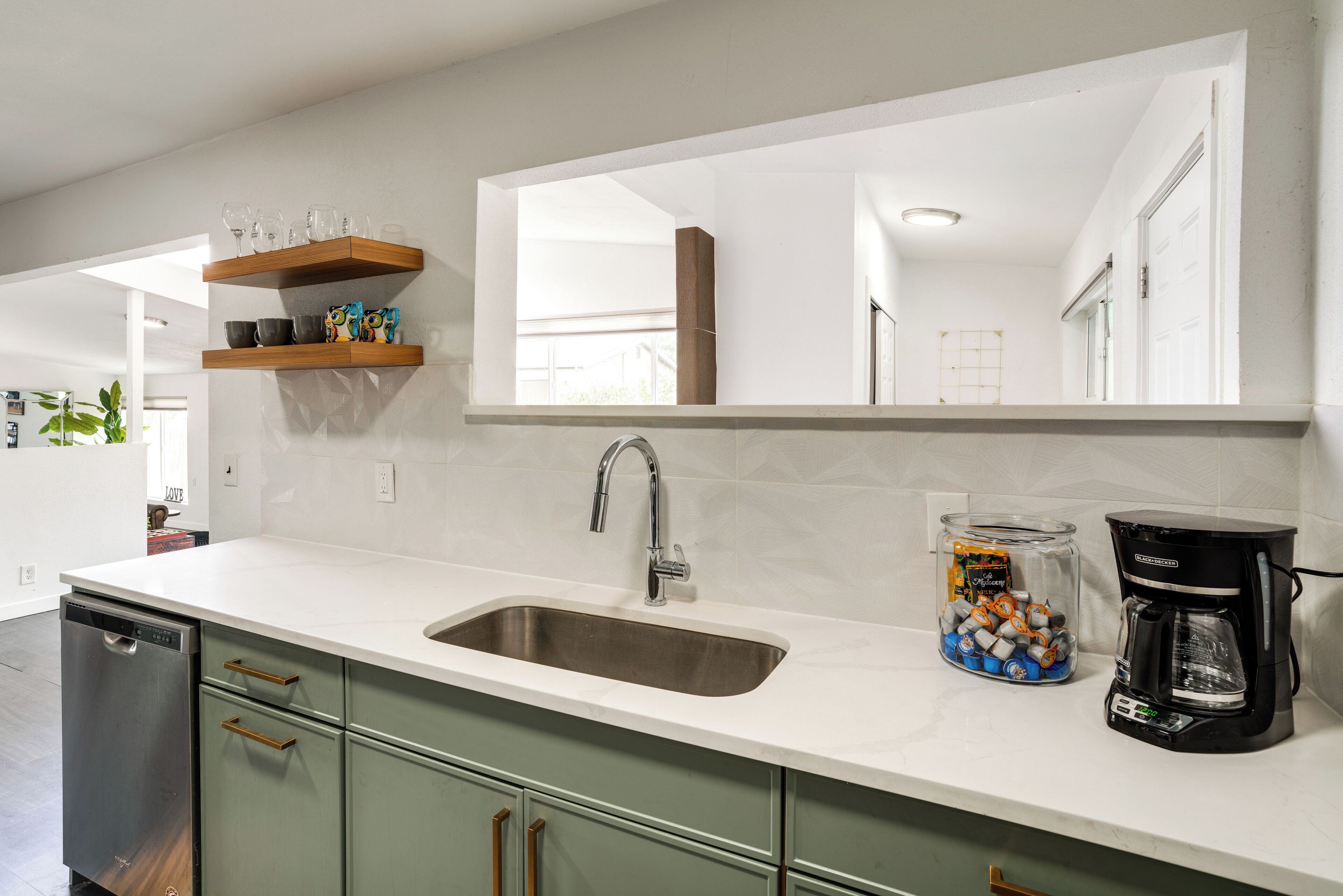 A kitchen with a built-in dishwasher, a sink, a coffee maker, and a shelf with glassware.