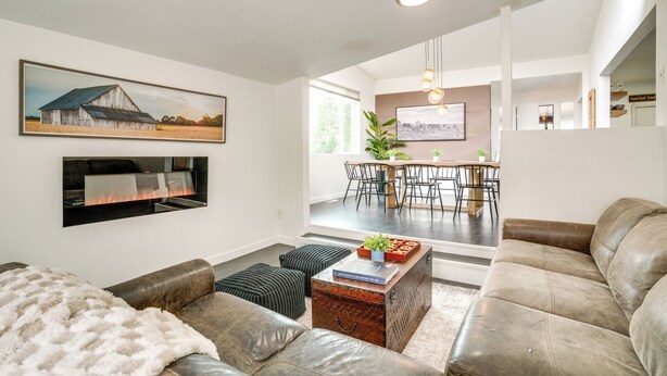 Una sala de estar moderna con chimenea, sofás de cuero, un comedor con mesa y sillas, y una cocina al fondo.
