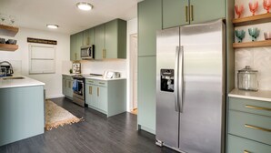 Una cocina moderna con armarios verde claro, electrodomésticos de acero inoxidable y encimera de madera.