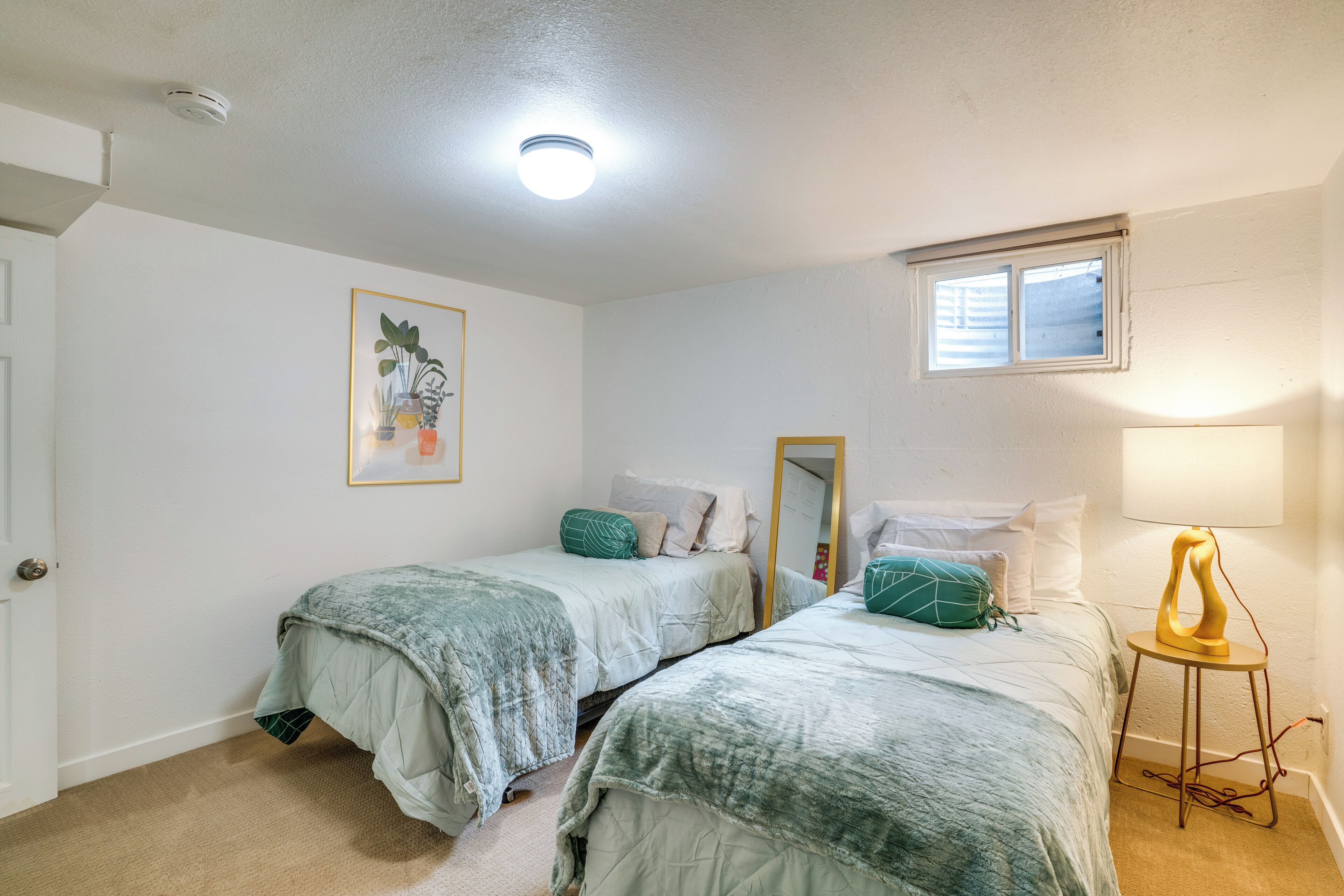 A bedroom with two beds, a window, a ceiling light, and a wall-mounted lamp.