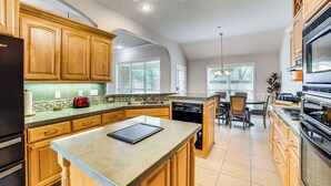 A kitchen with wooden cabinets, a refrigerator, a dishwasher, and a dining area with chairs and a table. - 8 Mi to Lake Palestine: Peaceful Family Retreat (Flint)