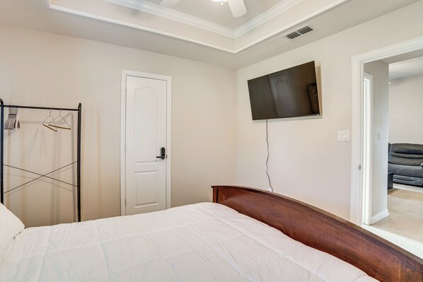 A bedroom with a bed, a TV mounted on the wall, and a door leading to another room.