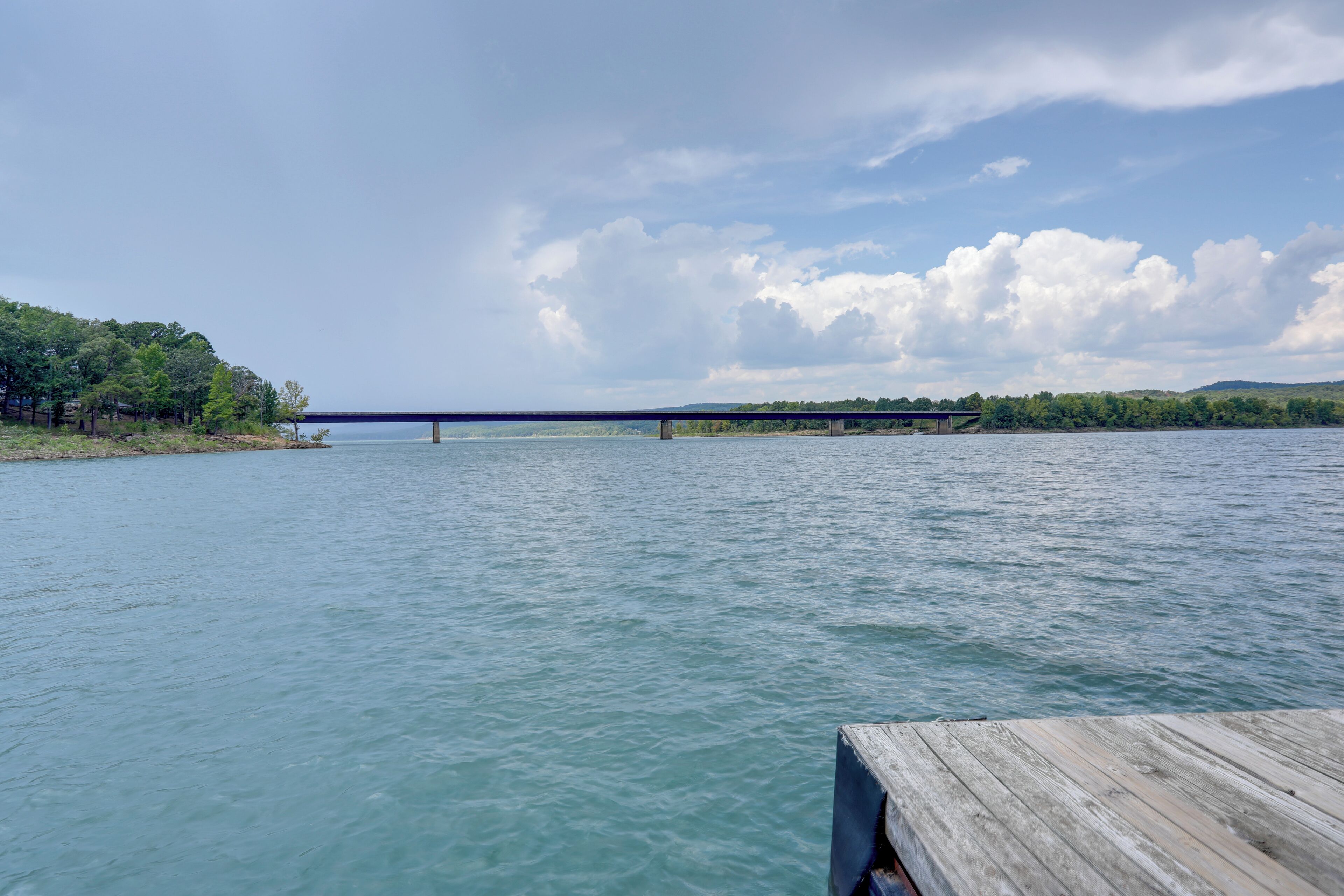 Une jetée en bois s’étendant dans une rivière paisible, avec un pont en arrière-plan.