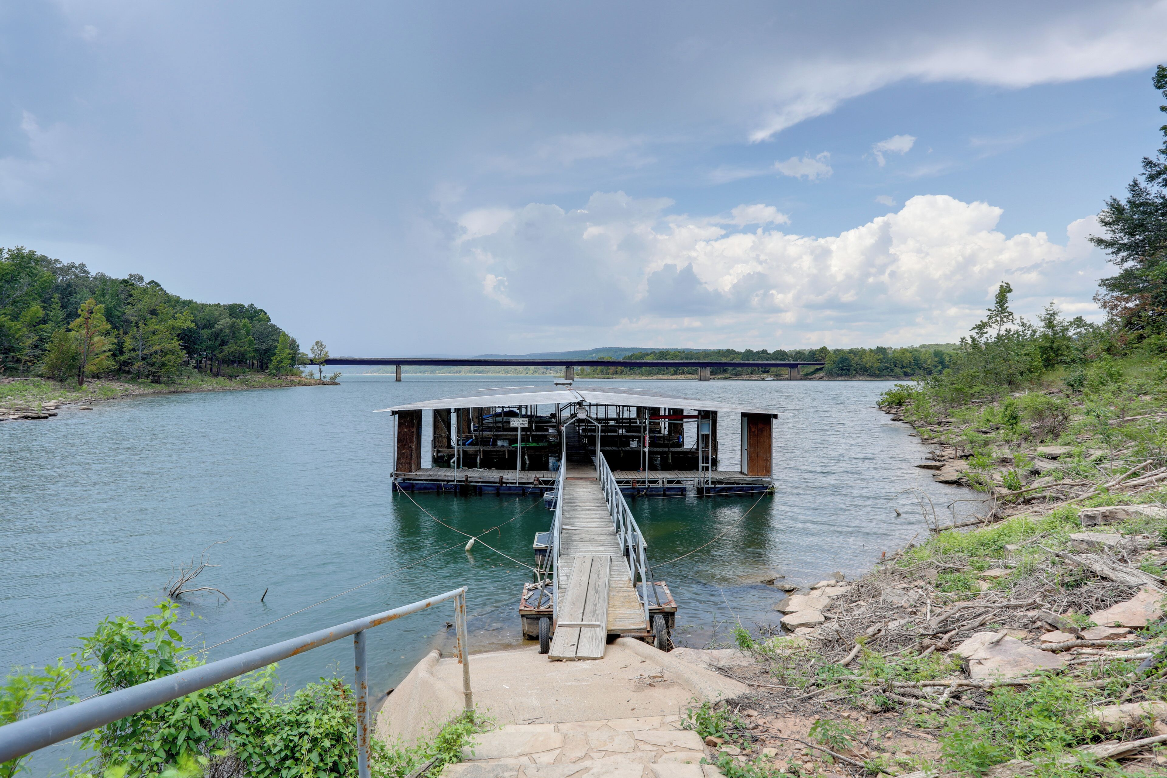 Eine Holzstele führt zu einer schwimmenden Plattform mit Überdachung, umgeben von ruhigem Wasser und viel Grün.