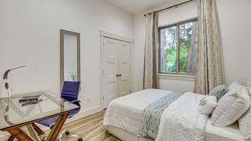 Ein Schlafzimmer mit einem Bett, einem Glastisch mit Stuhl, einem Kleiderschrank und einem Fenster mit Vorhängen.