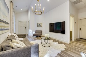 A modern living room with a sectional sofa, a round coffee table, a white shag rug, a mounted TV, and a chandelier. - Wfh-friendly Gem w/ Creek: 4 Mi to Sammamish Trail (Redmond)