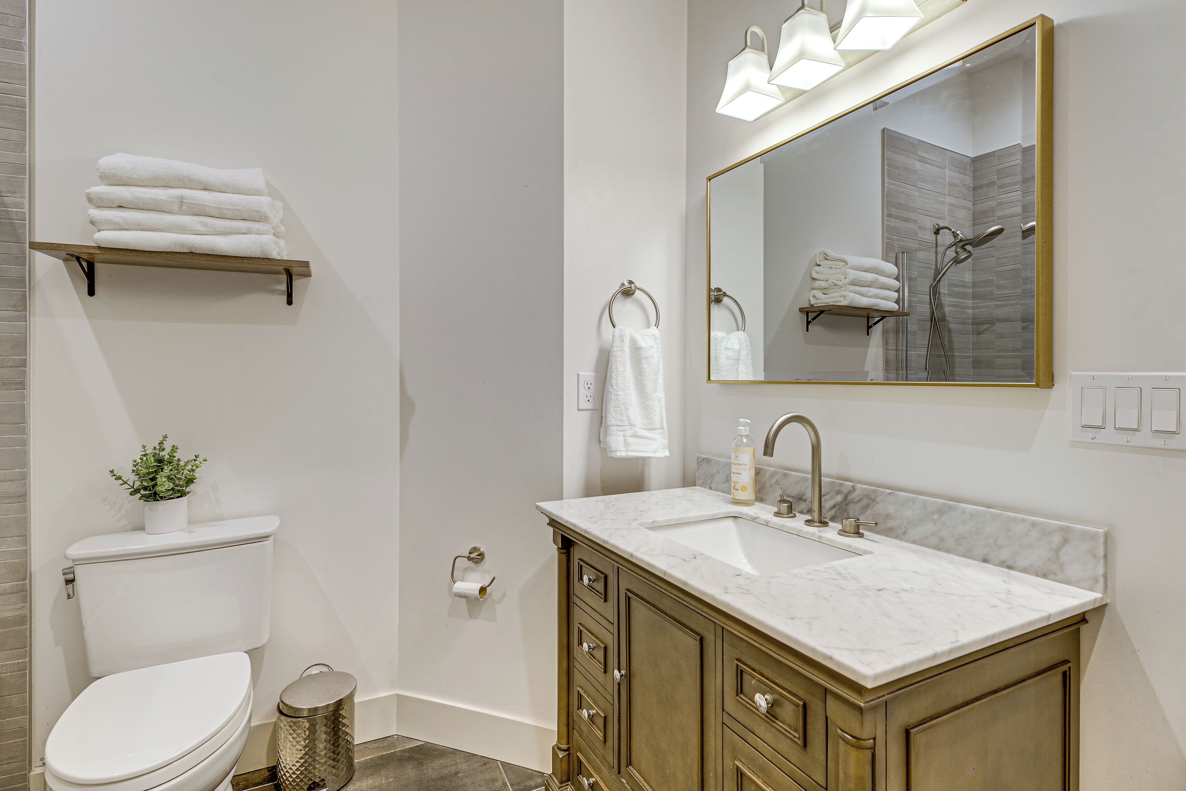 A modern bathroom with a toilet, sink, vanity, and a large mirror.