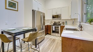 A modern kitchen with white cabinets, stainless steel appliances, a glass dining table, and two bar stools. - Wfh-friendly Gem w/ Creek: 4 Mi to Sammamish Trail (Redmond)