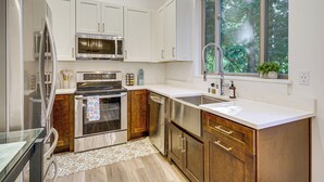 A modern kitchen with stainless steel appliances, wooden cabinets, and a large window providing a view of the outdoors. - Wfh-friendly Gem w/ Creek: 4 Mi to Sammamish Trail (Redmond)