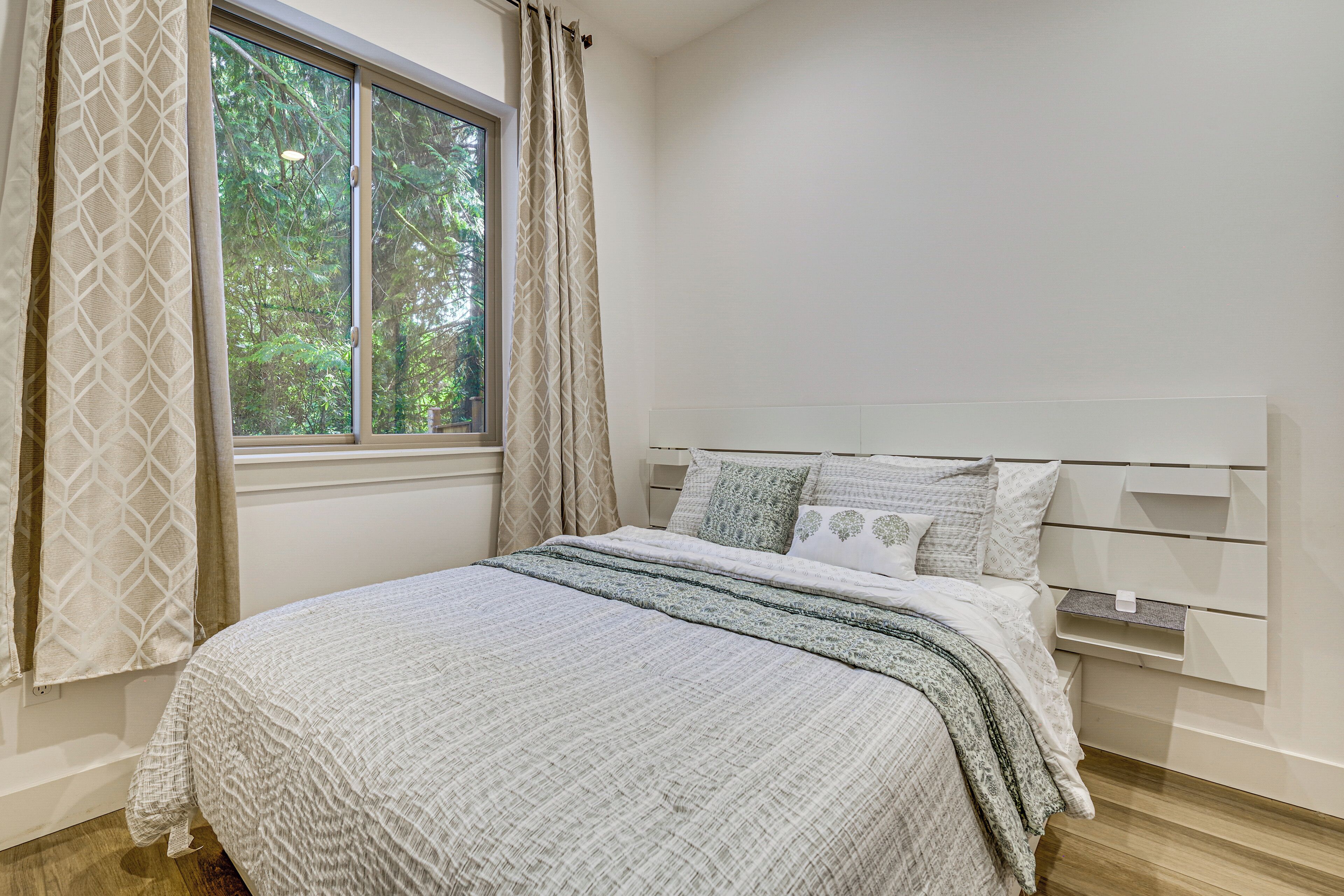 A bedroom with a bed, a window, and a bedside table.