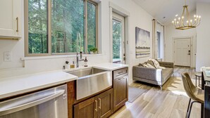 A modern kitchen with a large window, a built-in dishwasher, and a dining area with a sofa and table. - Wfh-friendly Gem w/ Creek: 4 Mi to Sammamish Trail (Redmond)