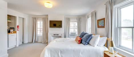 A bedroom with a bed, a television, a fireplace, and a window with curtains.