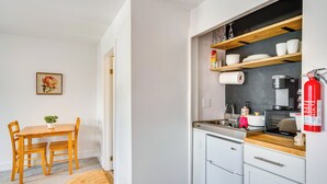 A compact kitchen with white cabinets, a wooden countertop, and a built-in oven. There is a dining area with a wooden table and chairs, and a small rug on the floor. - Waterbury Studio 12 Mi to Bolton Valley Ski Resort (Waterbury)