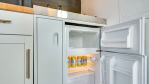 Ein weißer Kühlschrank mit einem separaten Gefrierfach oben und einer Ablagefläche darunter, auf der sich vier Dosen befinden.