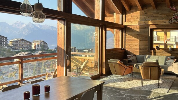 A spacious room with a wooden ceiling, large windows offering mountain views, a dining area with a table and chairs, and a cozy seating area with a sofa and armchairs. - Grimpeur 9 ski in/out, Spa Access (Haute-Nendaz)