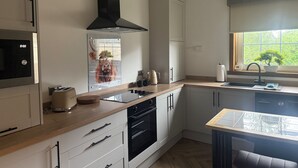 A modern kitchen with a built-in oven, a black range hood, and a window with a view of greenery. - Modern, Stylish Flat on Baker Street — 5 mins walk to Stirling Castle (Stirling)