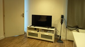 Een kamer met een televisie op een witte dressoir, een stofzuiger en een deur.